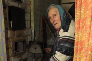 Eine alte Frau mit Kopftuch vor ihrem Ofen.