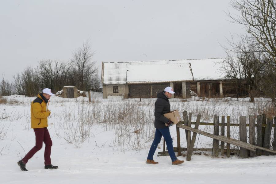 Zwei Männer gehen durch eine verschneite Landschaft zu einem Haus.