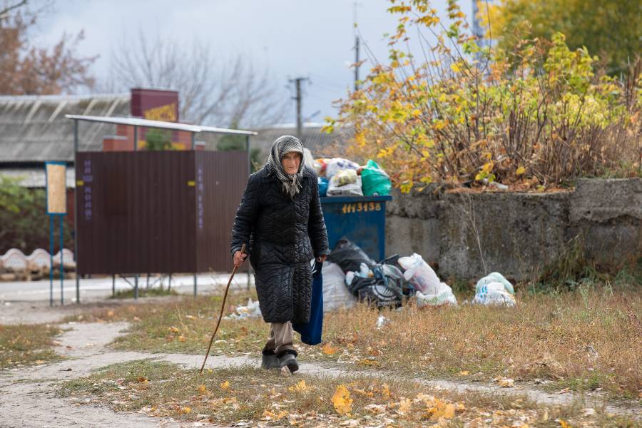 Eine alte Frau geht an einem Gehstock in der Nähe einer Straßein Borivske, die von Müllsäcken gesäumt ist.