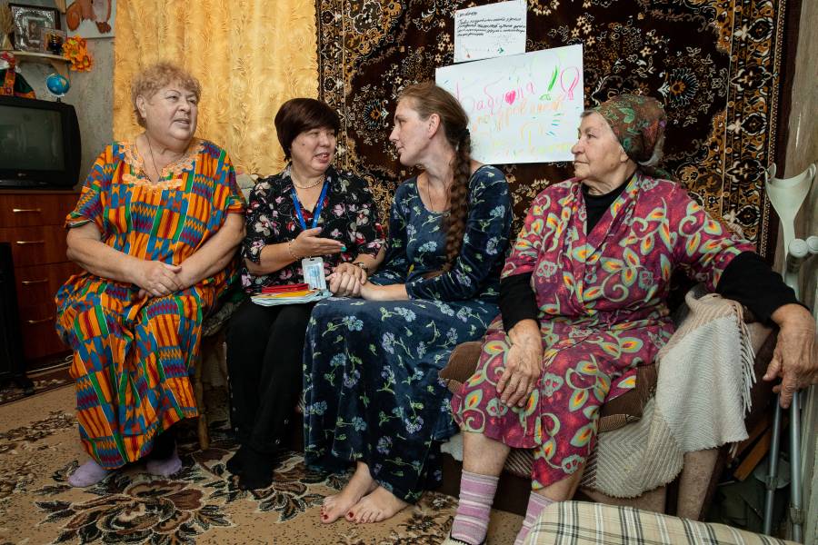 Elena Makaiya zusammen mit einer Mitarbeiterin der Caritas Ukraine, ihrer Mutter und ihrer Großmutter auf einer Couch im Wohnzimmer des gemeinsamen Hauses sitzend.
