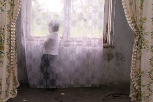 Ein kleiner Junge steht hinter einem Vorhang und schaut aus dem Fenster.