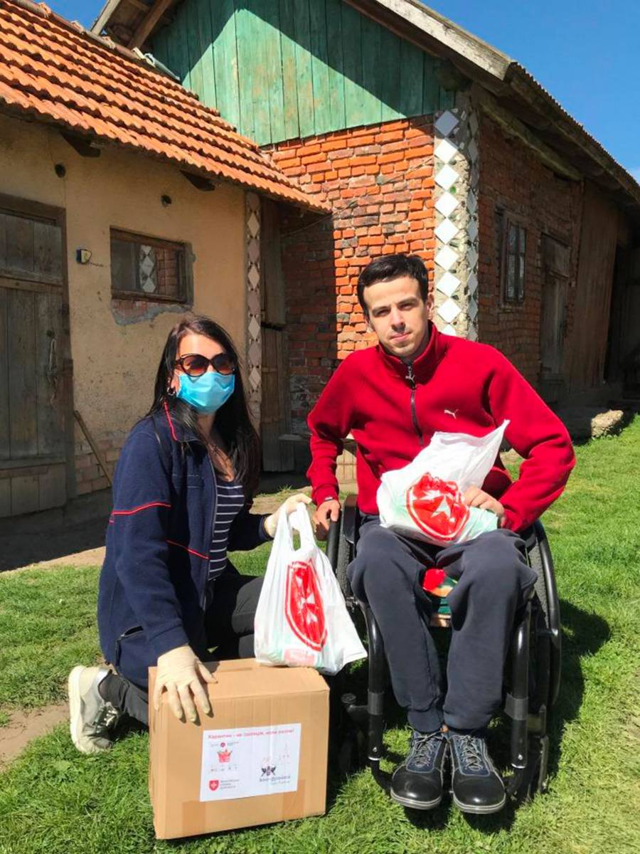Eine junge Helferin bringt Hilfspakete zu einem jungen Mann im Rollstuhl