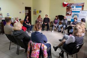 15 Personen sitzen nebeneinander in einem Stuhlkreis und tauschen sich im Rahmen der wöchentlichen Gesprächsgruppe für Binnenflüchtlinge im Caritaszentrum in Saporischschja aus.