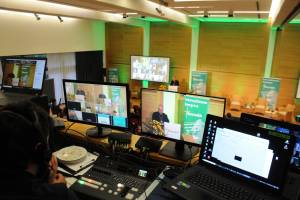 Mehrere aufgeklappte Laptops und im Hintergrund ein kirchlicher Würdenträger auf dem Podium.