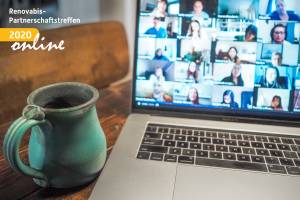 Kaffeetasse und aufgeklappter Laptop mit Online-Meeting
