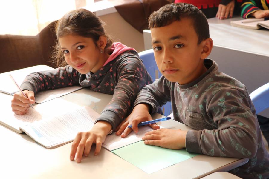 Zwei Schulkinder an einem Tisch mit Unterrichtsmaterial vor ihnen.