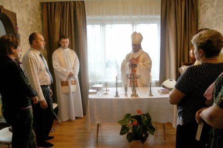 Eine kleine Gemeinde hat sich in einem Wohnzimmer zur Eucharistiefeier versammelt.