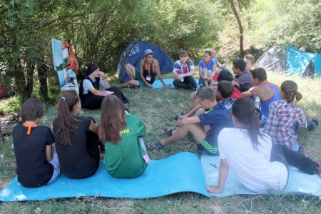 Gruppe von Jugendlichen sitzt auf einer Wiese und hört einer Ordensschwester zu.