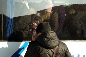 Frau mit Kind in einem Evakuierungsbus in der Ukraine, der Mann steht weinend davor