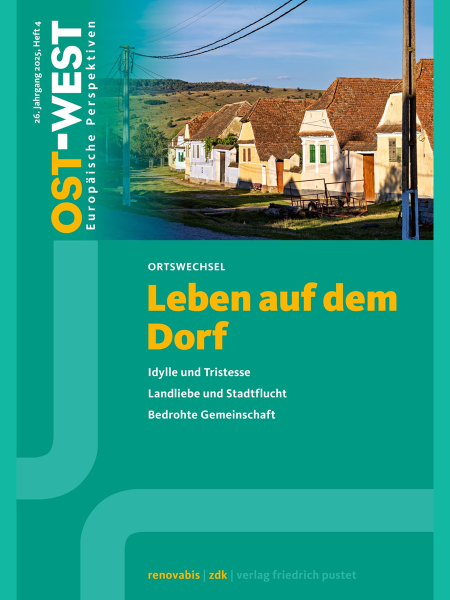 Straßenanansicht in einem von hügeliger Landschaft umgebenen Dorf mit einer Reihe einfacher Wohnhäuser. Vor den Häusern sieht man landwirtschaftliches Gerät und einen kleinen Wasserkanal entlang der Straße. Jedes Haus hat einen eigenen Zuweg, der jeweils mit einer kleinen Brücke über den Kanal zum Eingang verläuft.