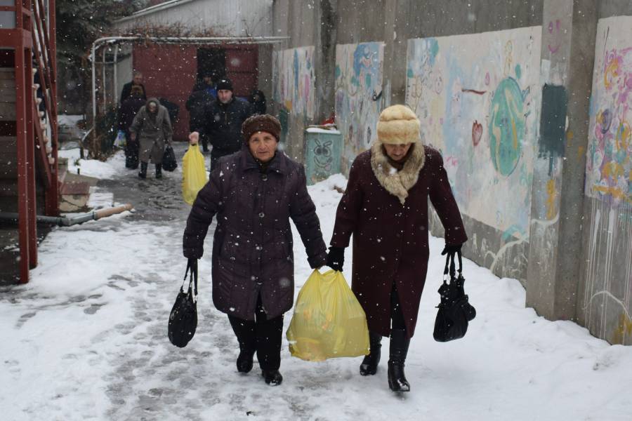 Zwei Frauen tragen gemeinsam einen Einkaufstüte auf einer verschneiten Straße.