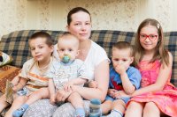 Mutter sitzt mit ihren vier Kindern auf einem Sofa.