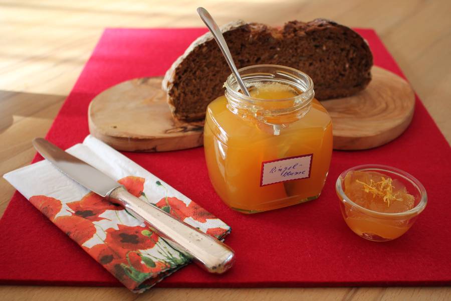 Ein Glas mit Ringelblumengelee auf einem Brettchen mit Brot und Besteck.