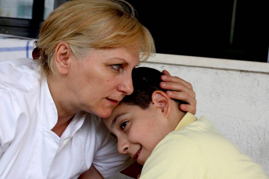 Eine Caritasmitarbeiterin umarmt einen Jungen mit Behinderung.