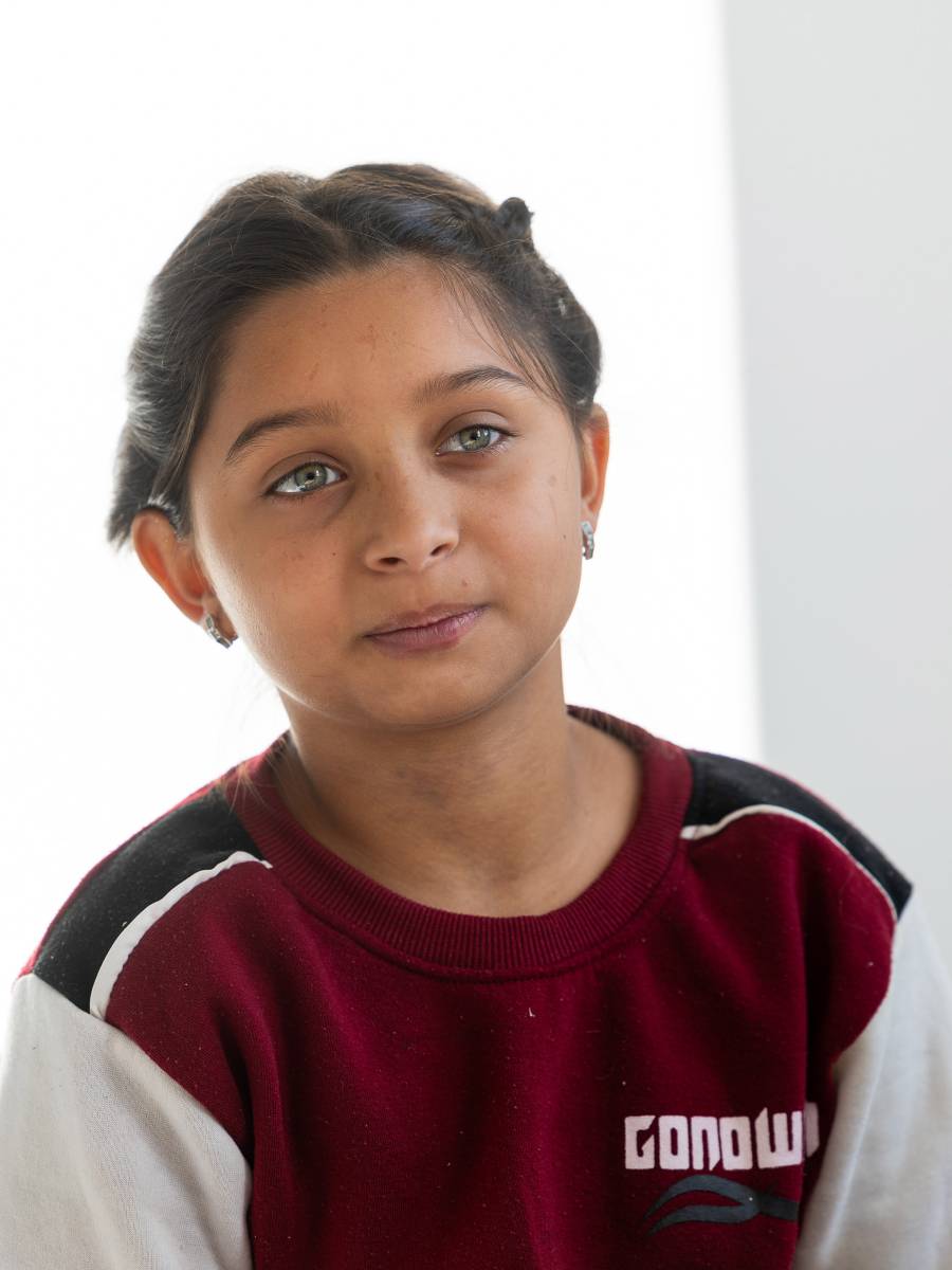 Das Bild zeigt ein etwa zehnjähriges Mädchen im rot-weißen Sweat-Shirt und mit strahlend grünen Augen, das an einem weißen Tisch sitzt.