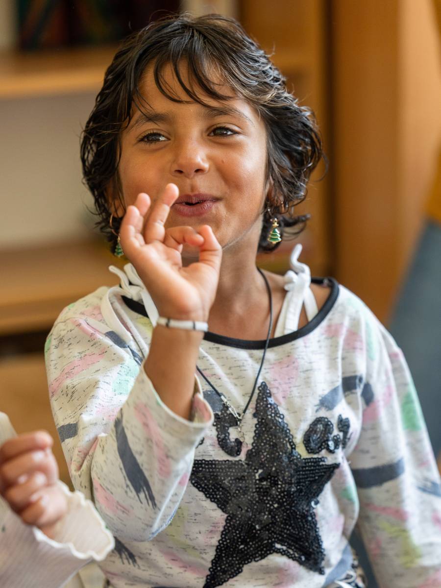Das Bild zeigt ein kleines Mädchen beim Spielen im Kindergarten des Ali-Ibra-Zentrums in Gjakove. Es trägt ein T-Shirt mit einem Glitzerstern, zwei funkelnde Ohrringe und freut sich sichtlich, mit anderen Kindern spielen zu können.