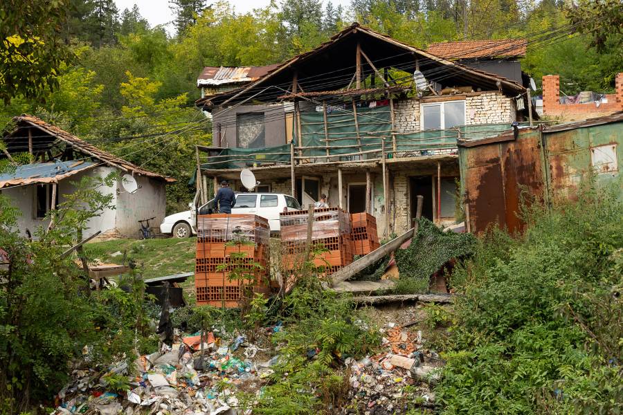 Ein Haus in der Roma-Siedlung in Malki Iskar. Die Ziegel sind unverputzt, das Haus wirkt windschief, es sind viele Stützpfeiler aus Holz und Metall zu sehen. Davor liegen neue Ziegelsteine, aber auch sehr viel Müll.