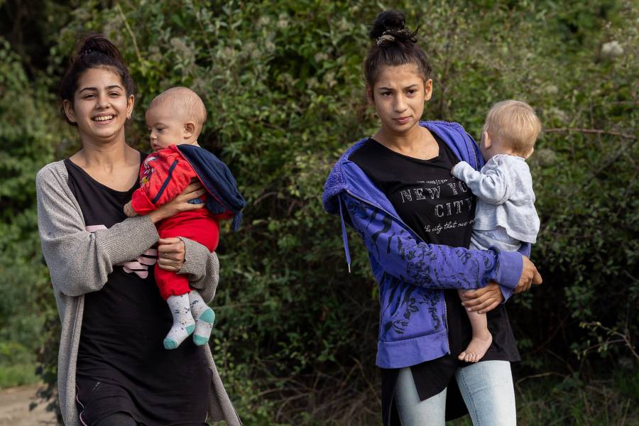 Zwei sehr junge Roma-Frauen laufen mit ihren Kleinkindern auf dem Arm durch die Roma-Siedlung in Malki Iskar. Beide Frauen tragen dunkle T-Shirts und darüber Strickjacken, eines der Kleinkinder hat keine Söckchen an.