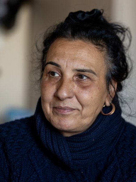 Porträt der Romnja Elena. Sie ist 56 Jahre alt und trägt einen dunkelblauen Strickpullover, die Haare hat sie im Nacken zu einem Dutt zusammengenommen, einzelne Strähnen umspielen ihr Gesicht.