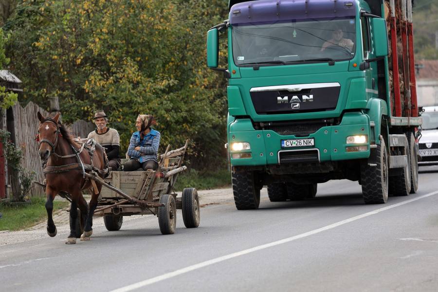 Eine Pferdefuhrwerk mit einem alten Mann und einer alten Frau auf dem hölzernen Wagen fährt auf einer Straße in Rumänien, dahinter ein großer grüner Lastwagen.