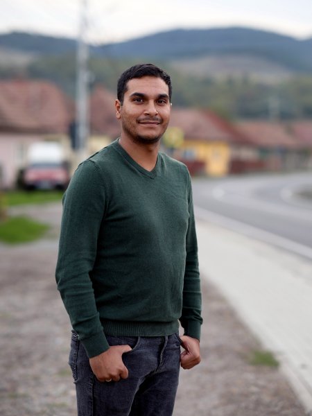 Ottó Kalányos - der häufig „Pap Bácsi“ genannt wird, Onkel Priester - steht am Rand einer Straße in Rumänien. Er trägt Jeans, einen waldgrünen Pullover, einen Drei-Tage-Bart und kurze, dunkle Haare.