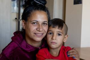Porträtaufnahme einer Mutter aus der Roma-Minderheit in Bulgarien, die ihren Sohn im Arm hat. Sie blickt lächelnd in die Kamera.