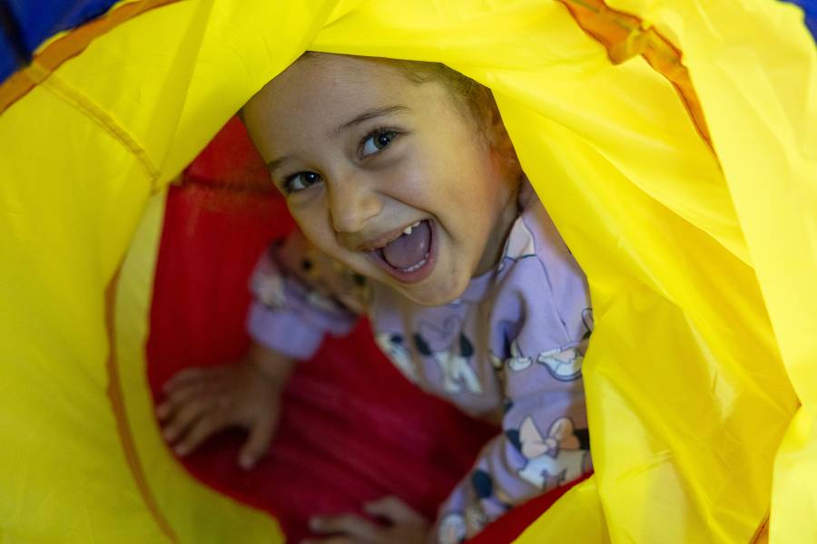 Ein junges Mädchen blickt lächeln durch einen gelben Kinder-Spieltunnel.
