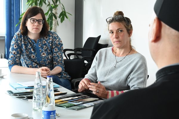 Das Bild zeigt die beiden Projektreferentinnen Christiana Hägele und Katharina Ebel, beide sitzen am Tisch und hören aufmerksam Bischofsvikar Mykhailo Klapkiv zu, der am rechten Bildrand zu sehen ist.