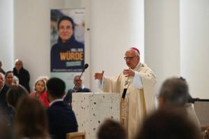 Erzbischof Dr. Heiner Koch steht am Altar der Sankt Hedwigs-Kathedrale in Berlin und spricht zu den versammelten Gläubigen. In liturgischem Gewand betont er mit einer ausdrucksstarken Geste seine Worte. Im Hintergrund ist ein Roll-up mit dem Motto der Renovabis-Pfingstaktion 2025 zu sehen: „Voll der Würde – Menschen stärken im Osten Europas“.