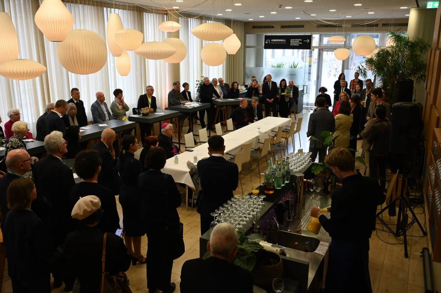 Eine große Gruppe von Männern und Frauen an Stehtischen im Quadriga-Forum in Berlin. Fast alle sind elegant gekleidet und tragen Anzug oder Jacket.