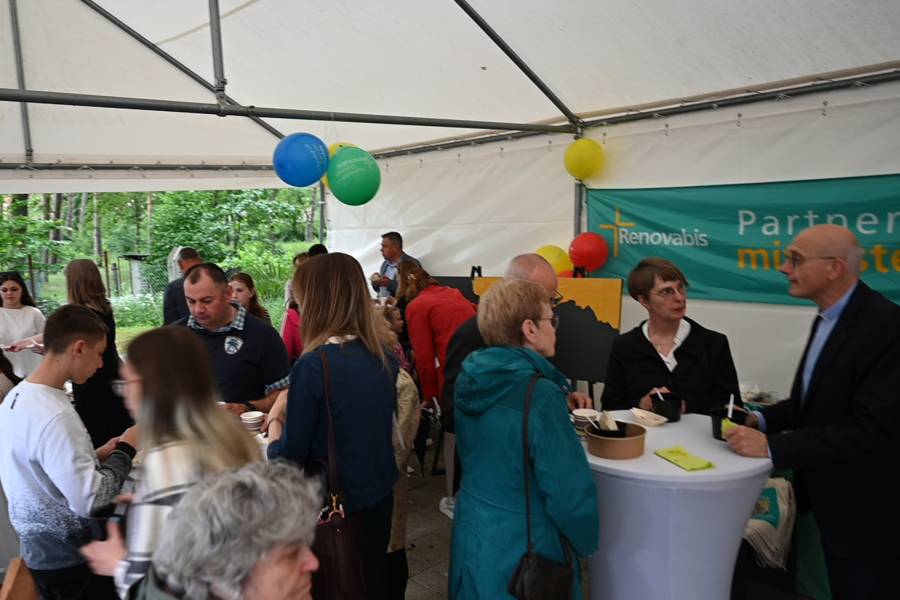In einem Zelt stehen an Stehtischen mit weißen Hussen viele Männer und Frauen, die gemeinsam essen und sich unterhalten. An der Decke schweben Luftballons, im Hintergrund hängt ein Renovabis-Banner.