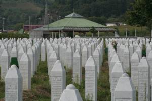 Das Bild zeigt eine große Menge weißer Grabsteine, die eng aneinander gereiht sind. Auf ihnen sind die Namen der Opfer des Genozid von Srebrenica zu lesen.