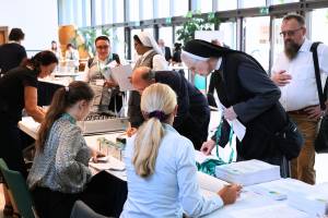 Participants are standing at a reception desk at the 29th International Congress Renovabis in Berlin, where information materials and conference documents were being distributed.