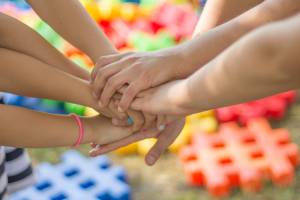 The photo shows a group of children's hands stacked together in a gesture of unity and teamwork.