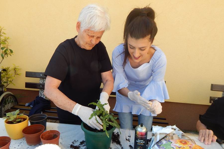 Eine Bewohnerin des Altenheims pflanzt mit der Betreuerin Blumen in einen Topf.