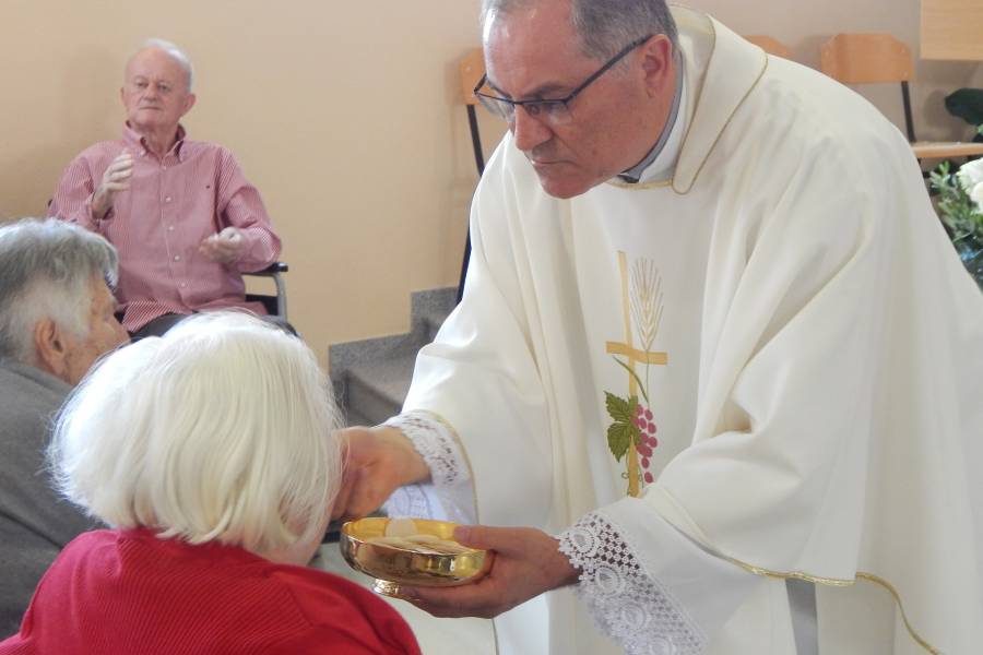 Pfarrer verteilt die Kommunion an eine Frau bei einem Gottesdienst im Altersheim.