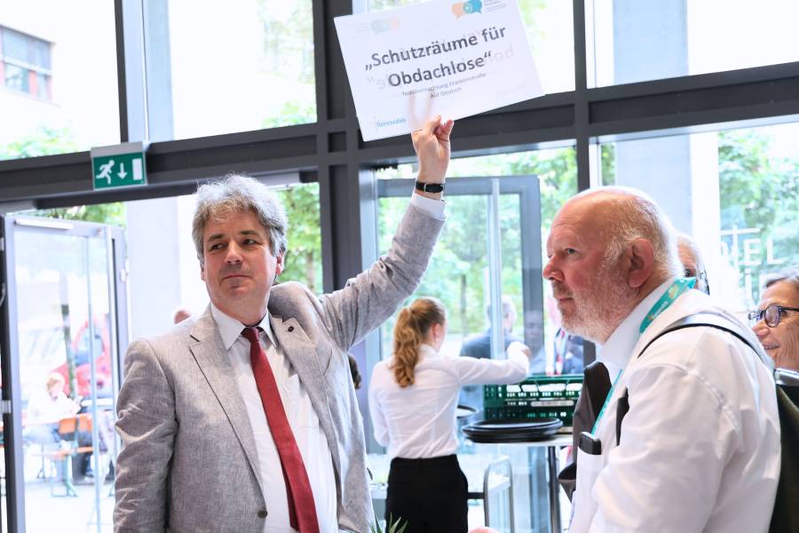 Dr. Markus Ingenlath hält ein Schild hoch mit der Aufschrift „Schutzräume für Obdachlose“ beim Renovabis-Kongress. Am Nachmittag des zweiten Kongresstages standen sieben Exkursionen auf dem Programm. Eine Gruppe unter Begleitung von Renovabis-Geschäftsführer Dr. Markus Ingenlath besuchte eine Notübernachtung in Berlin.<br><small class="stackrow__imagesource">Quelle: Doris Breitsameter, Renovabis </small>