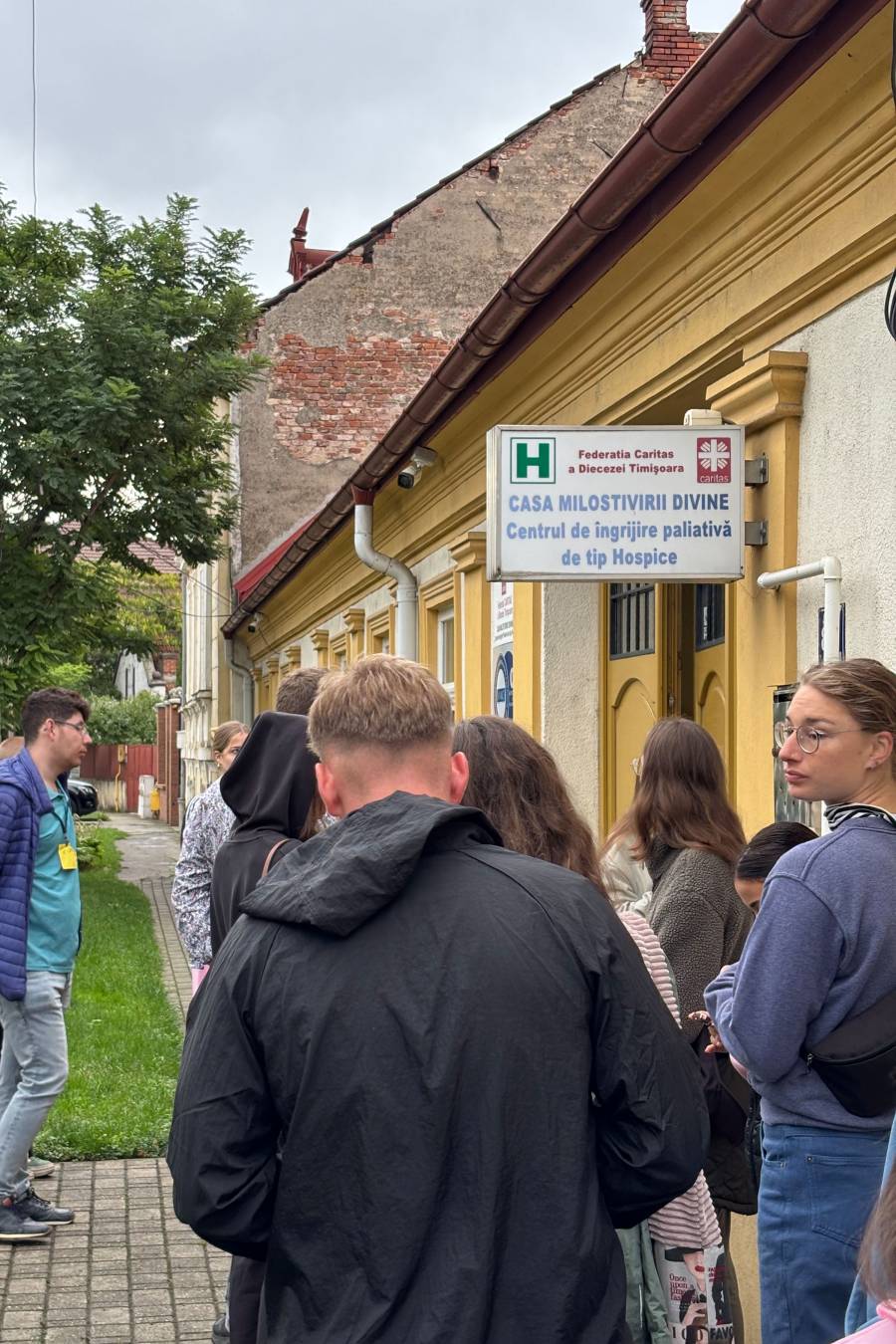 Ein gelbes Gebäude - das Hospiz in Timișoara -, davor stehen einige Teilnehmende der Jugendbegegnung.