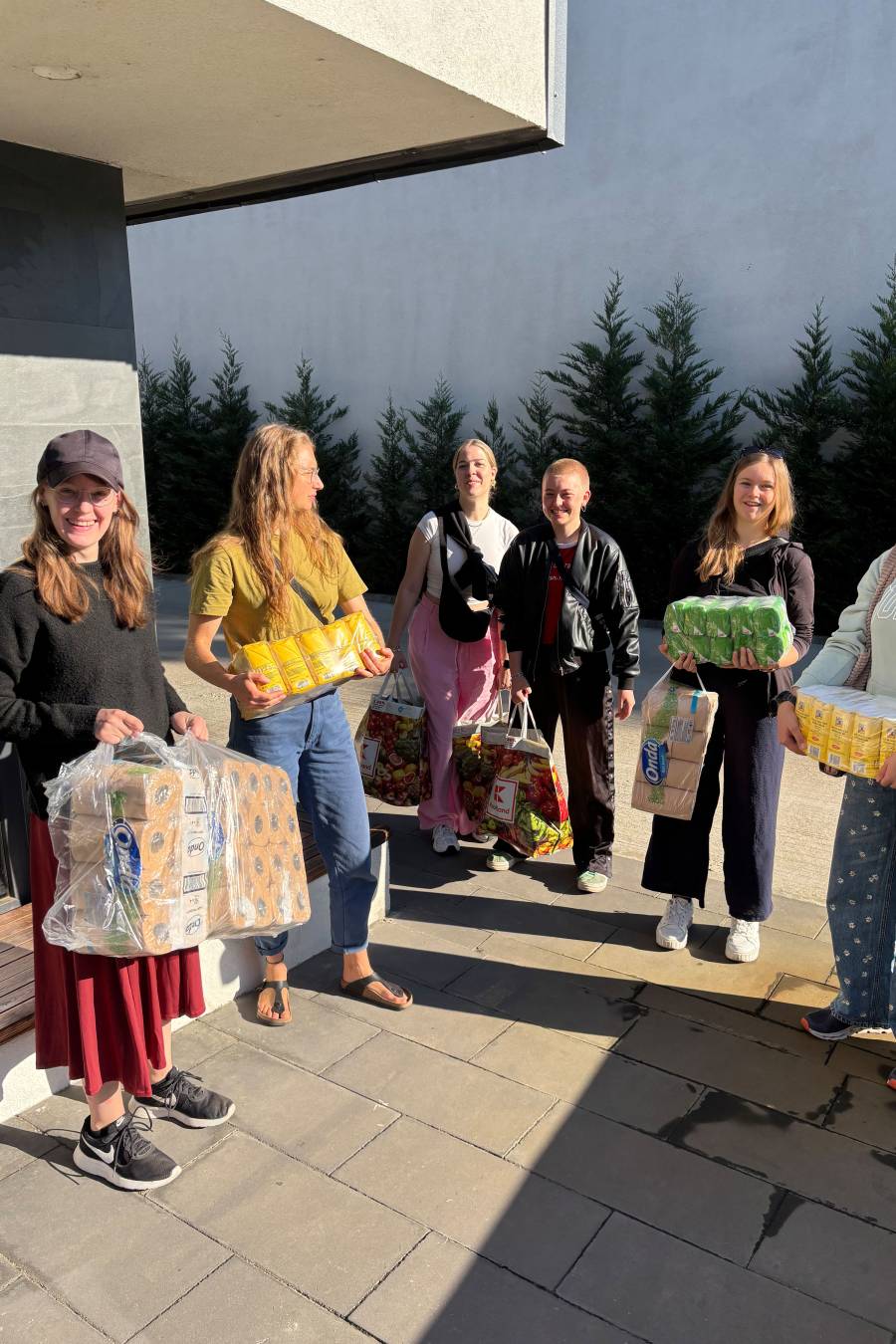 Junge Menschen mit vielen Einkäufen, darunter große Pakete mit Toilettenpapier