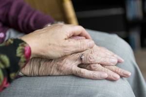 Das Bild zeigt die Hand einer alten Person, auf der die Hand einer jüngeren Person ruht.