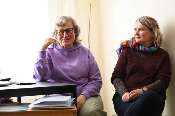 Das Bild zeigt zwei Damen, die an einem Tisch sitzen. Die Dame links spricht gerade.
