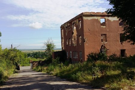 Von Bomben zerstörtes Haus in einer grünen Landschaft.