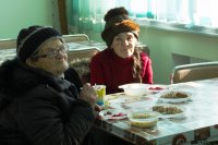 Zwei Frauen sitzen in der Suppenküche in Mariupol am gedeckten Tisch.