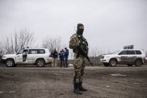 Soldat mit Waffe, im Hintergrund Mitglieder der OSCE Special Monitoring Mission