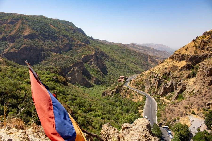 Eine bergige Landschaft in Armenien mit der Flagge des Landes und einer Straße, die sich durch die Hügel windet.