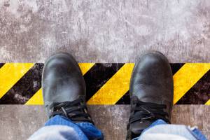 Schwarze Sicherheitsschuhe auf einem Betonboden mit gelb-schwarzer Warnmarkierung.