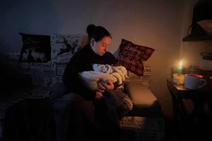 Eine Frau sitzt in einem dunklen Raum und hält ein kleines Baby in ihren Armen. Erhellt werden beide nur vom Schein einer Kerze.