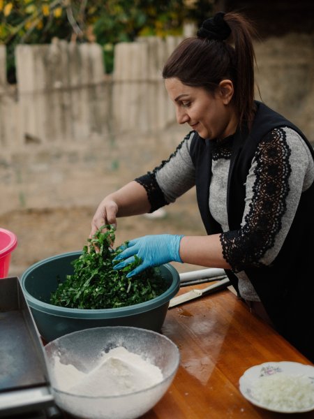Gohar Sargsyan mit einer Schüssel voller grüner, geschnittener Kräuter und Gemüse und einer weiteren Schüssel mit Mehl - den Zutaten für Jingalov Hats, den traditionellen armensischen Fladenbroten mit Kräuterfüllung.