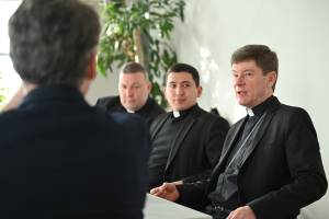 Das Bild zeigt den Bischof am rechten Rand in einem schwarzen Priester-Gewand. links neben ihm sitzen zwei weitere Personen. Am rechten Rand ist der Hinterkopf von Dr. Markus Ingenlath zu sehen, der dem Bischof zuhört.