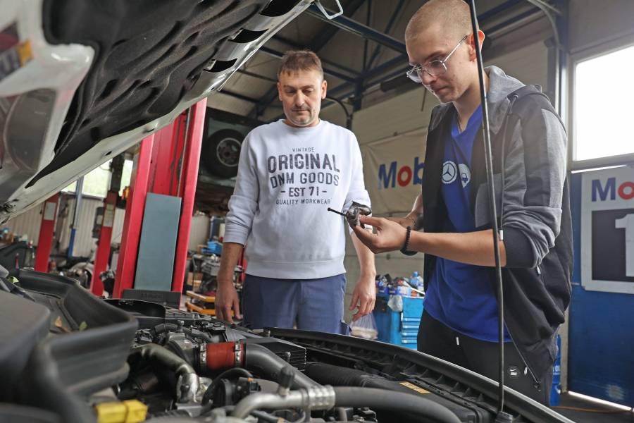 Aleksa Božović steht zusammen mit seinem Chef Daniel Jovin vor einer geöffneten Motorhaube in der Werkstatt.